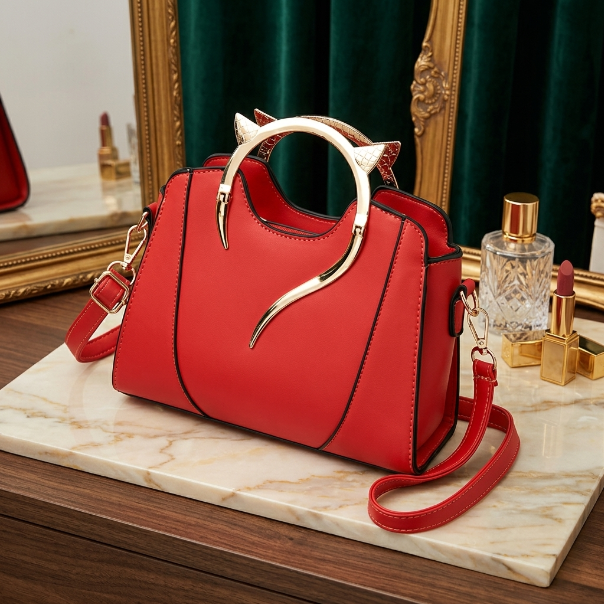 Red handbag with gold accents on a marble surface, with a mirror and perfume bottle in the background.