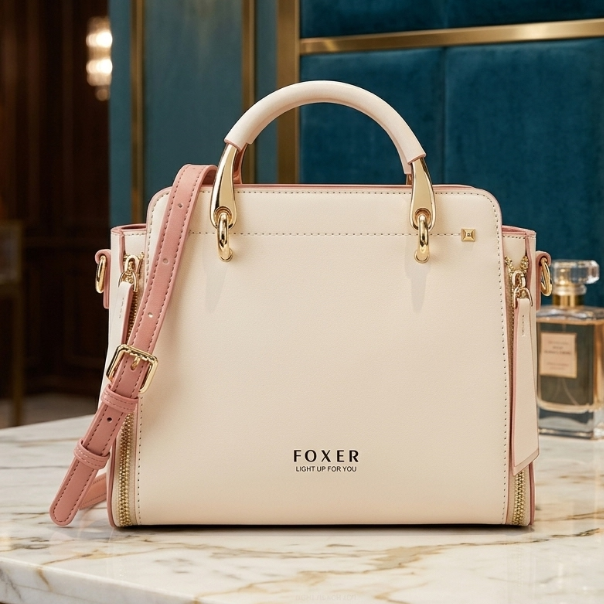 Beige handbag with pink strap and gold accents on a marble surface, next to a perfume bottle.